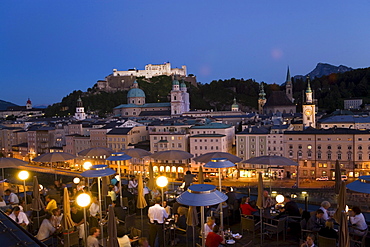 View over illuminated roof deck of restaurant Hotel Stein to old town with Salzburg Cathedral, St. Peter's Archabbey, Franciscan Church, City Hall Tower and Hohensalzburg Fortress, largest, fully-preserved fortress in central Europe, in the evening, Salzburg, Salzburg, Austria, Since 1996 historic centre of the city part of the UNESCO World Heritage Site