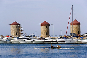 Women rowing in the Mandraki harbour (translated literally: fold), anchoring ships and windmills on mole in background, Rhodes Town, Rhodes, Greece