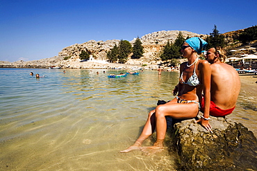 Couple sitting on rocks and talking, Saint Paul's Bay (Agios Pavlos), Lindos, Rhodes, Greece