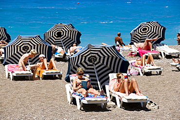 People sunbathing on sunloungers at main beach, Rhodes Town, Rhodes, Greece