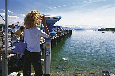 Woman looking through telescope at lake, Lake Starnberg, Bavaria, Germany