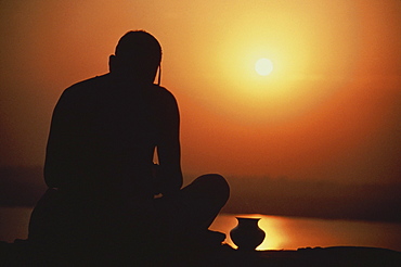 Silouette of a man praying with vase, India