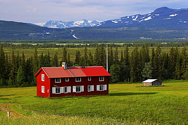 Red wooden house and view at snowcovered mountains near Klocka at the Annsjoen, Jaemtland, northern Sweden