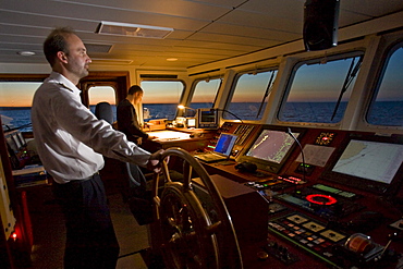 Captain at the helm and helmsman in training on the bridge of a ship, on the Hanse Explorer in the evening, Great Britain