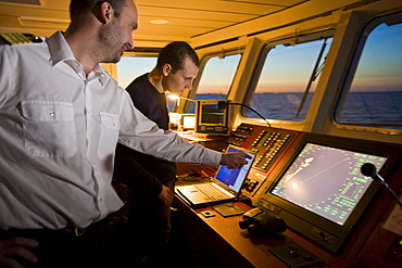 Captain and helmsman in training on the bridge of a ship, Hanse Explorer, in the evening light, Great Britain