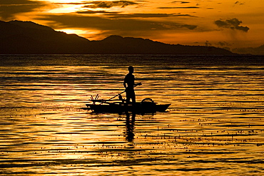 Man standing paddling in a canoo at sunset, New Britain, Papua New Guinea, Oceania