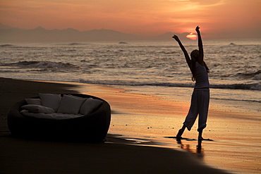 A young woman doing exercises on the beach at sunset, near Uluwatu, Bali, Indonesia