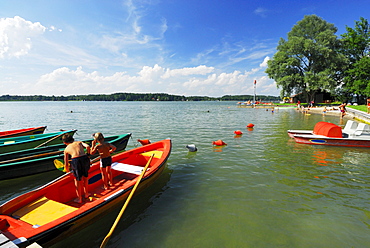 Two children fishing on rowing boat at beach of lake Simssee, Chiemgau, Upper Bavaria, Bavaria, Germany