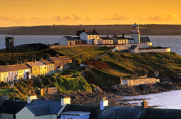 Houses and lighthouse on shore in the light of the evening sun, Roche's Point, County Cork, Ireland, Europe