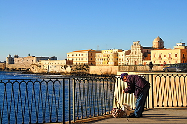 Angler with the houses of Siracusa in the background, at Lungomare, Siracusa