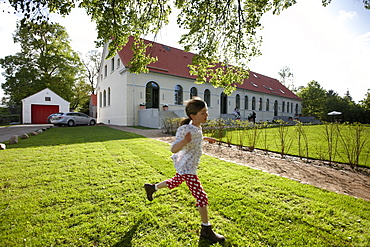 Girl running over a meadow near an hotel, Fincken, Mecklenburg-Western Pomerania, Germany