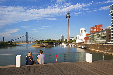 Couple sitting on a bridge at media harbour, view to Rhine tower and Neuer Zollhof, Duesseldorf, North Rhine-Westphalia, Germany, Europe