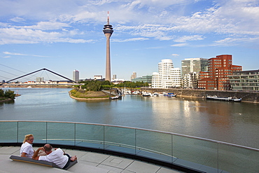 Couple sitting on a terrace at media harbour, view o Rhine tower and Neuer Zollhof with Gehry buildings, Duesseldorf, North Rhine-Westphalia, Germany, Europe