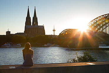 Young woman sitting on the Rhine river banks opposite to the cathedral, Cologne, North Rhine-Westphalia, Germany, Europe