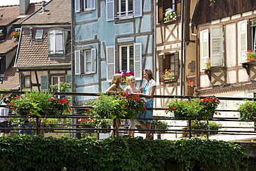 Mother and two daughters standing on a bridge in front of half-timbered houses in Petite Venise, Colmar, Alsace, France