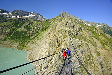 Hikers walking over a suspension bridge across a mountain lake, Trift glacier, Trift suspension bridge, Tieralplistock, Urner Alps, Bernese Oberland, Bern, Switzerland