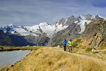 Woman and man hiking near a mountain lake with view to Mischabel range with Allalinhorn, Alphubel, Taeschhorn, Dom and Lenzspitze, Pennine Alps, Valais, Switzerland