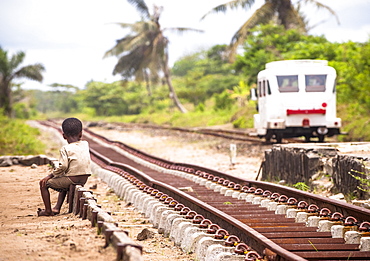 Child sitting on the edge of railway lines, looking at a train, Madagascar, Africa