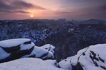 Sunset above the Saxon Switzerland national park with a wide view from Carolafelsen above the heavily snow covered landscape, Saxony, Germany