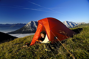 Young woman looking out of a tent in the mountains, Tyrol, Austria, Europe