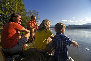 Family sitting on the shore of lake Staffelsee, near Murnau, Upper Bavaria, Bavaria, Germany