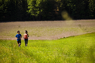 Two joggers running over a meadow, Upper Bavaria, Germany