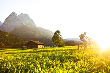 Mountain biker passing meadow with hay barns, Grainau, Bavaria, Germany