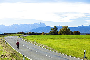 Woman jogging along a road, Munsing, Bavaria, Germany