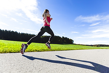 Woman jogging along a road, Munsing, Bavaria, Germany