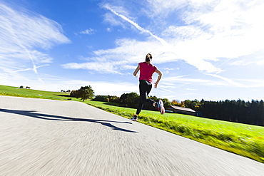 Woman jogging along a road, Munsing, Bavaria, Germany