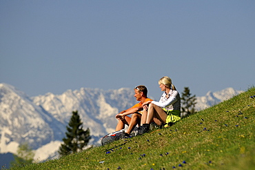 Couple sitting on a mountain pasture admiring the view, Wallgau, Karwendel, Upper Bavaria, Bavaria, Germany, Europe