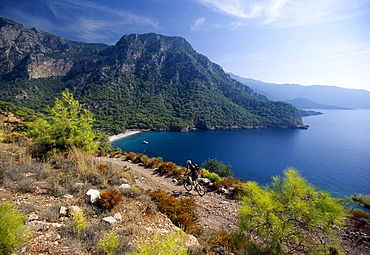 Mountain biker in front of Kabak Beach in a bay, Lycian coast, Turkey, Europe