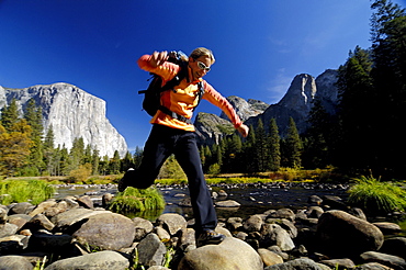 Woman wearing rucksack jumping over stones at brookside, Yosemite National Park, California, North America, America