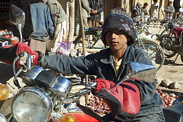 Boy sitting on a parked motorcycle at the bazaar in Bamiyan, Bamian Province, Afghanistan