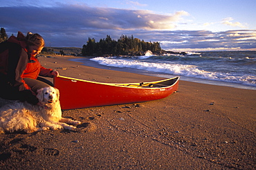 Woman and Dog sit by Canoe beside Lake Superior, Northern, Ontario