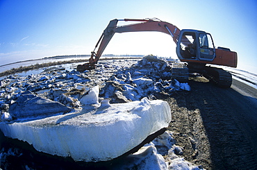 A Front Shovel Excavator unblocking Ice buildup which has caused Flooding of Agricultural Land during Spring Runoff, near Dugald, Manitoba