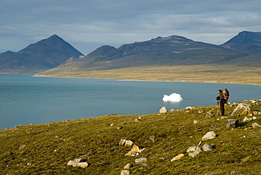 Man in arctic landscape with iceberg in background, Baffin Island, Nunavut, Canada