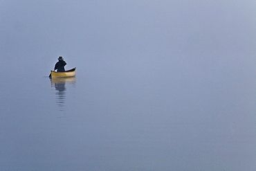 Woman paddling canoe in morning mist, Algonquin Park, Ontario