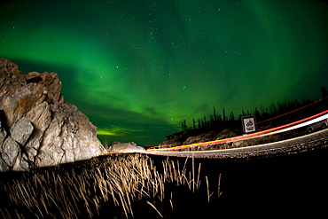 Lights of a passing vehicles under Aurora Borealis at the start of the Ingraham Trail, outside Yellowknife, Northwest Territories