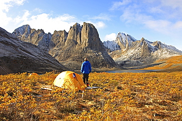 Camper standing by his tent at sunrise over Divide Lake with Mount Monolith in background, Yukon