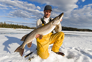 Man Ice Fishing holding a Northern Pike, Wawa, Ontario