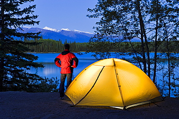 Hiker by a tent looking out at Boya Lake at dusk, Boya Lake Provincial Park, Northern British Columbia