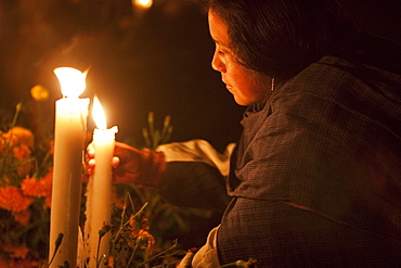 Woman arranging candles on a grave during the celebration of Dia de los Muertos, the Day of the Dead at the San Pedro Cucuchucho cemetery. People decorate the graves of their loved ones with offerings of flowers, particularly marigolds (cempoalxochitl or zempasuchil), bread of the dead (pan de muerto), candles, the deceased's favourite food, drinks and personal belongings to guide their spirits home. Families celebrate their late relatives by the tombs all night from November 1, All Saints Day to November 2, All Souls Day., Michoacun, Mexico