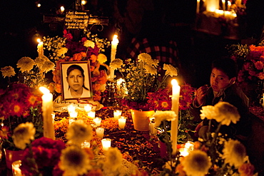 Boy by his mother's grave during the celebration of Dia de los Muertos, the Day of the Dead at the San Pedro Cucuchucho cemetery. People decorate the graves of their loved ones with offerings of flowers, particularly marigolds (cempoalxochitl or zempasuchil), bread of the dead (pan de muerto), candles, the deceased's favourite food, drinks and personal belongings to guide their spirits home. Families celebrate their late relatives by the tombs all night from November 1, All Saints Day to November 2, All Souls Day., Michoacun, Mexico