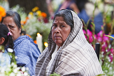 Woman by a grave during the celebration of Dia de los Muertos, the Day of the Dead at the San Jeronimo Purenchecuaro cemetery. People decorate the graves of their loved ones with offerings of flowers, particularly marigolds (cempoalxochitl or zempasuchil), bread of the dead (pan de muerto), candles, the deceased's favourite food, drinks and personal belongings to guide their spirits home. Families celebrate their late relatives by the tombs on November 2, All Souls Day., Michoacun, Mexico