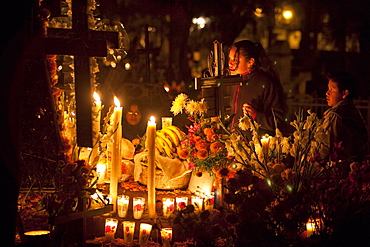 Grave of a teenager shot in a hunting accident during the celebration of Dia de los Muertos, the Day of the Dead at the Tzintzuntzan cemetery. People decorate the graves of their dead children, often referred to as little angels (angelitos) with offerings of flowers, particularly marigolds (cempoalxochitl or zempasuchil), bread of the dead (pan de muerto), candles, toys, the deceased's favourite food, drinks and personal belongings to guide their spirits home. Families celebrate their late offspring by the tombs all night from October 31 to November 1, All Saints Day, date that is set aside for remembrance of deceased infants and children., Michoacun, Mexico