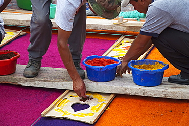 People working on a carpet made of sand & sawdust along the Good Friday processional route. Carpet-making is thought of as a sacrificial act, as the elaborate detail and time that go into the carpet making is a way for people to give something of themselves in memory of the crucifixion of Jesus. These carpets last on average 2 hours before they are destroyed by the many feet that march over them during a procession in Antigua Guatemala., Sacatepuquez, Guatemala