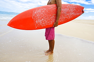 Hawaii, Kauai, Man holding surfboard on beach, View from side.