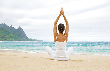 Hawaii, Kauai, Haena Beach Tunnels Beach, Woman meditating on sandy shore.