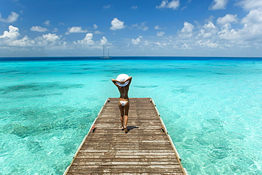 Woman walking to end of tropical ocean pier, View from behind.